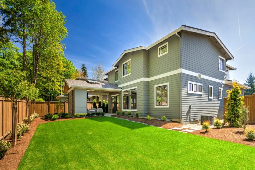 Large modern grey new house with open backyard with cut grass and minimal tress and shrubbage.  