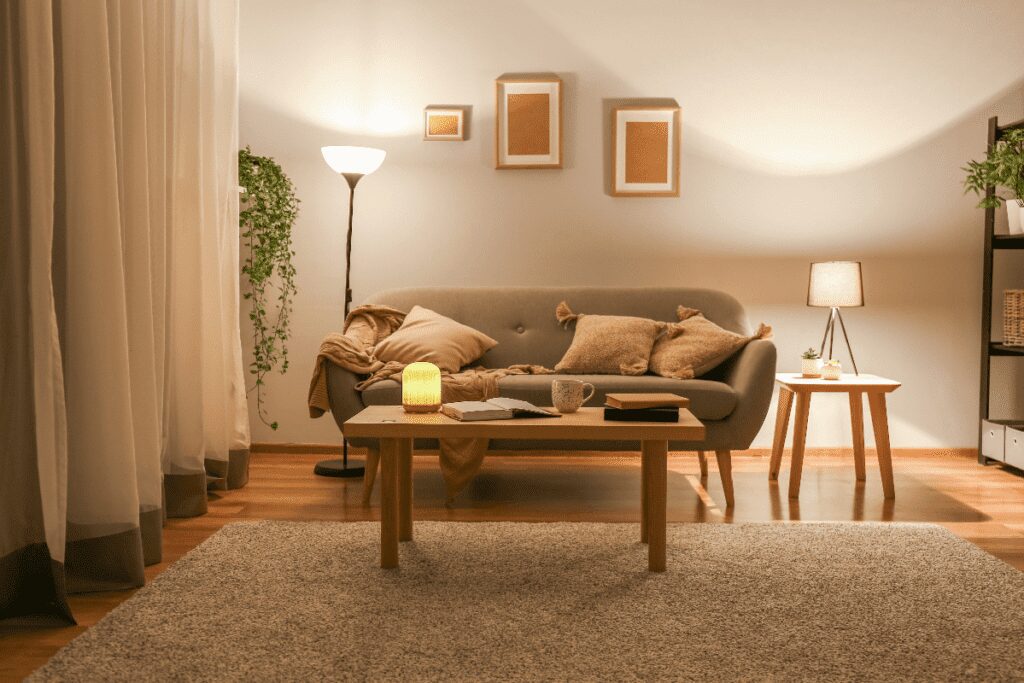 Small living room lit only with end table lamp and floor lamp, both with  white shades.