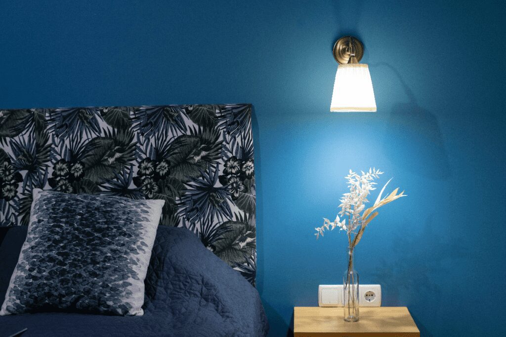 Cobalt colored bedroom wall with wall light next to headboard and above nightstand.