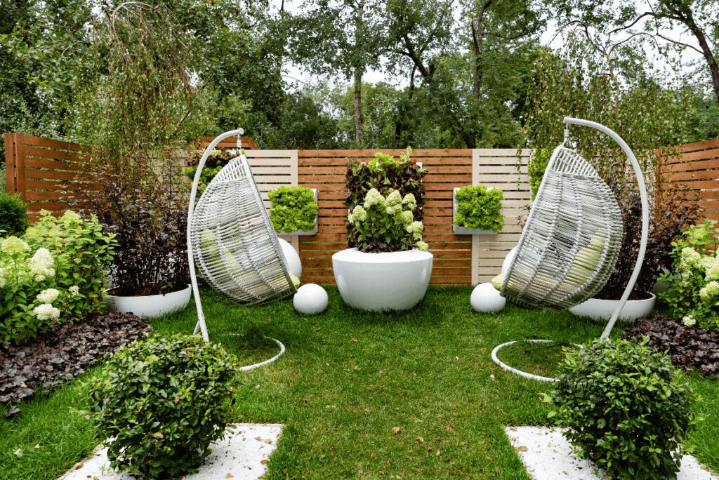 Backyard area filled plants and flower pots with two hanging chairs in center.