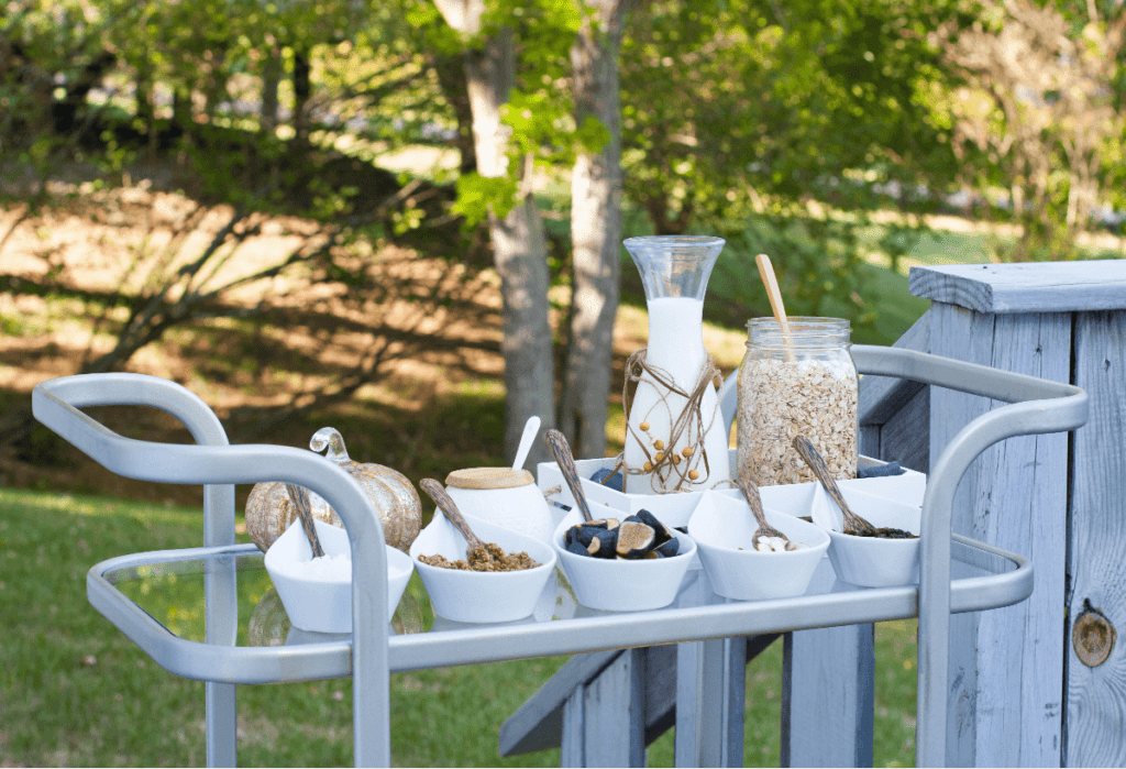 Bar cart on a deck/patio, filled with casters for a brunch buffet of granola, milk, and assorted toppings.