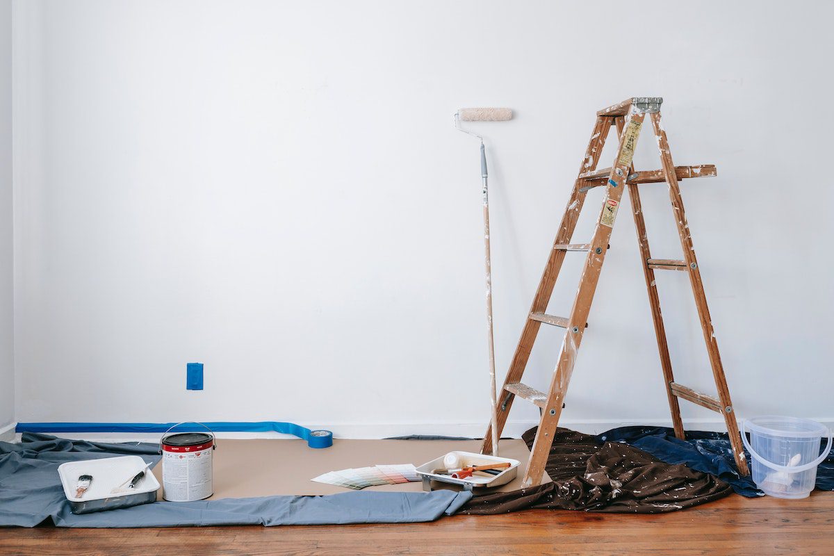 View of a ladder and house painting materials against a blank wall.